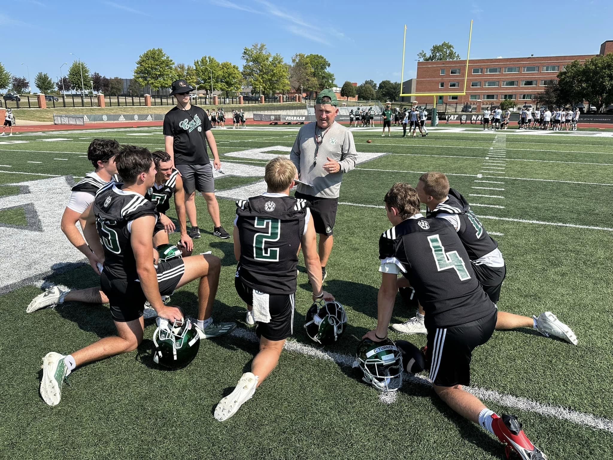 Northwest Missouri State quarterbacks talk with offensive coordinator Todd Sturdy following the first practice on August 5.